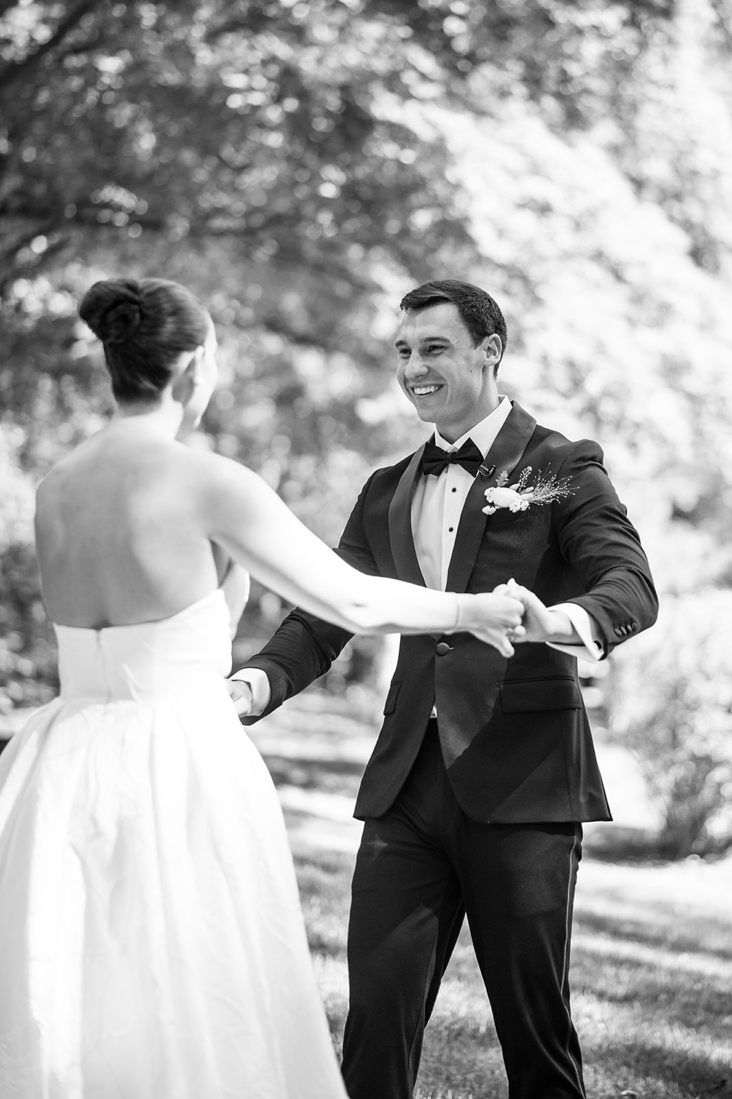 Black and white portrait of a groom holding the bride's hands and smiling affectionately during their first look.